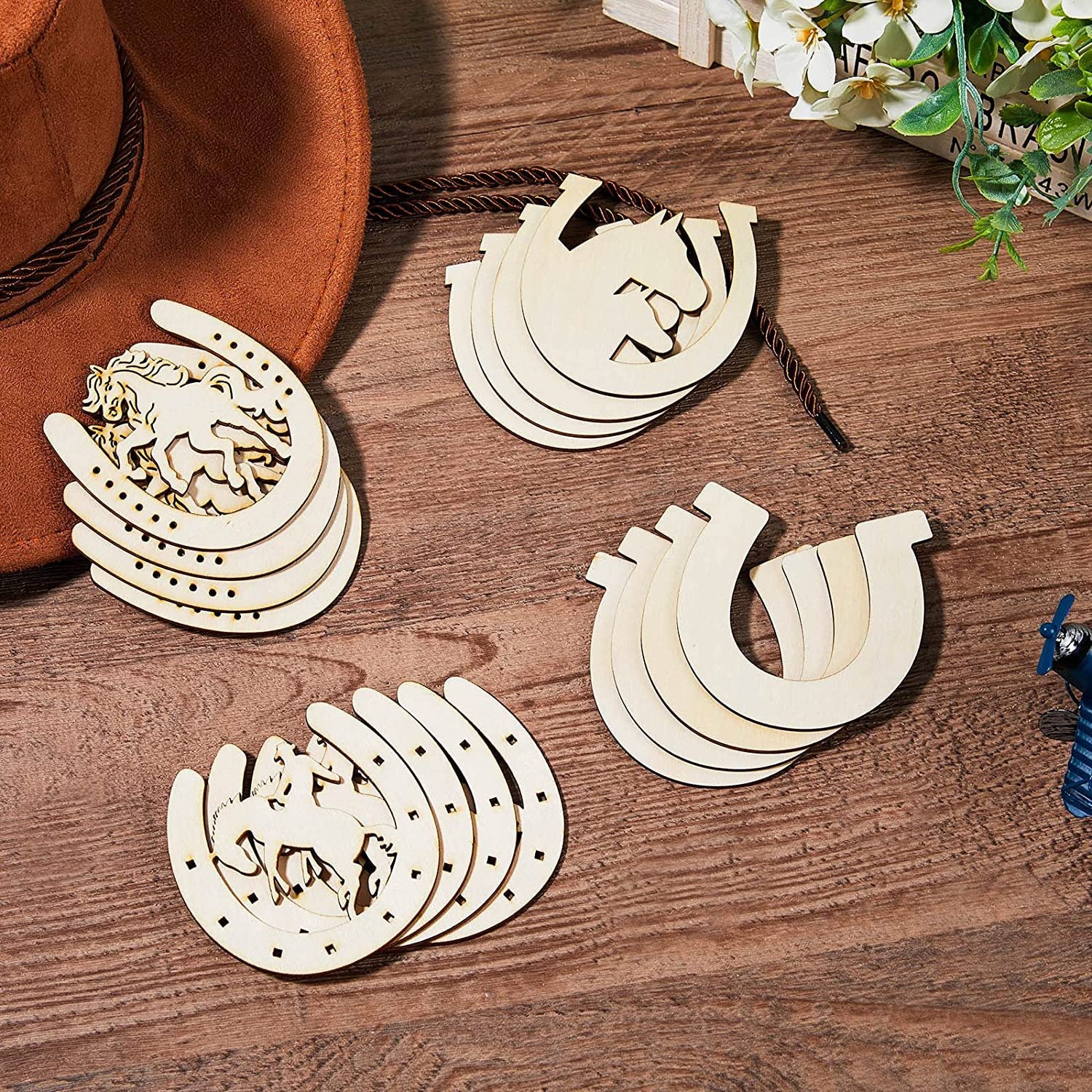 Wooden horse shoe decorations on a wooden surface with a hat and flowers in the background.