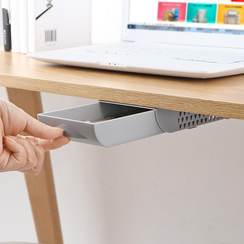 Hand opening a small drawer attached to a desk with a laptop in the background.