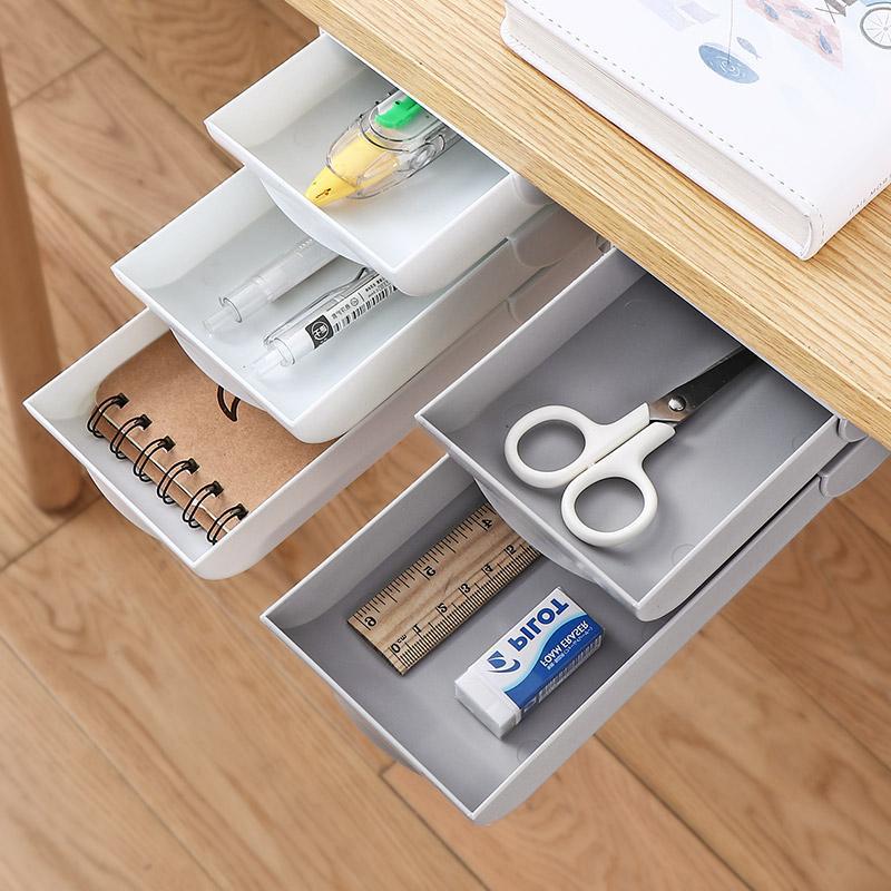 Open drawer with stationery items including scissors, ruler, and eraser on a wooden desk.