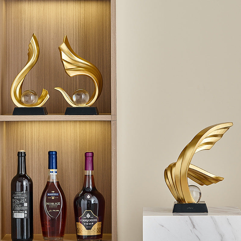 Decorative gold sculptures on a shelf with wine bottles below.