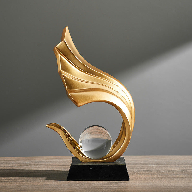 Gold decorative sculpture with a glass ball on a wooden surface and gray background