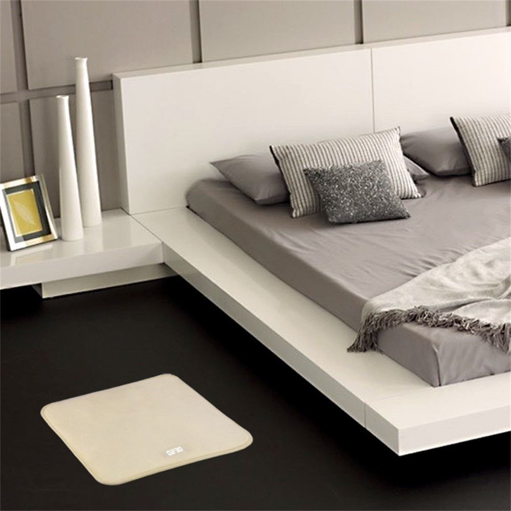 Beige bath mat in front of a bed with gray bedding in a modern bedroom.