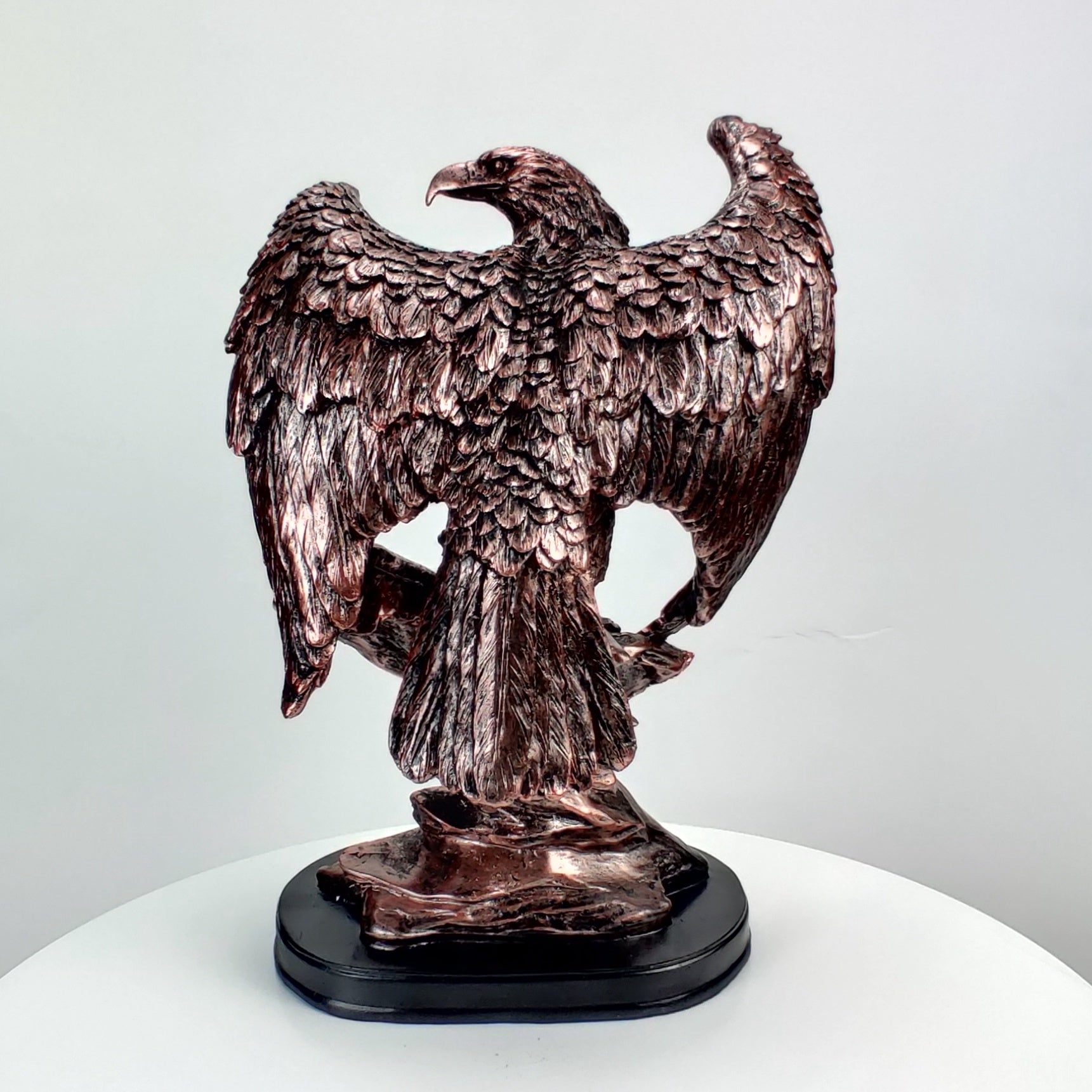 Bronze statue of an eagle on a white pedestal with a light gray background