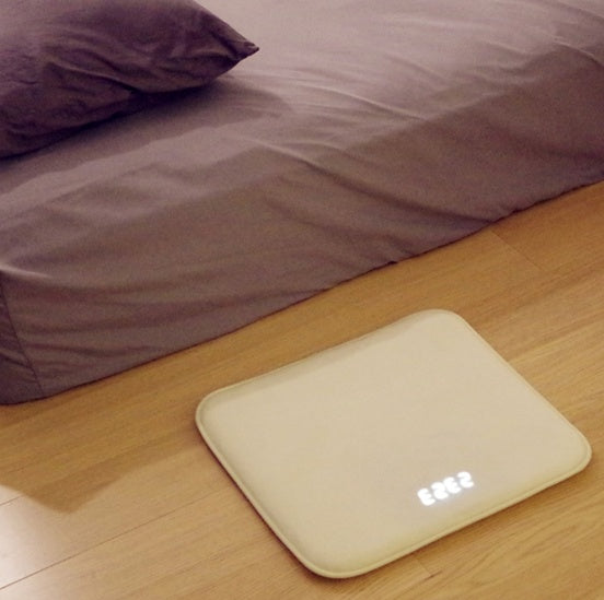 White electronic device on a wooden floor with a bed in the background
