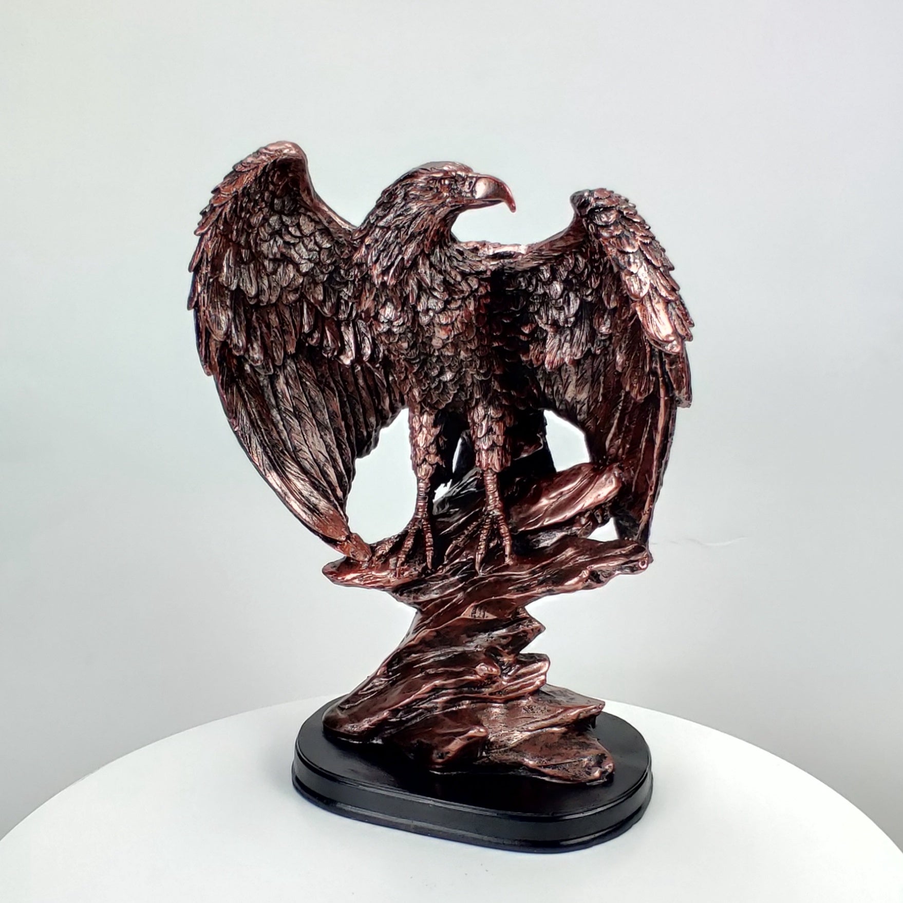 Bronze statue of an eagle on a white pedestal with a light gray background