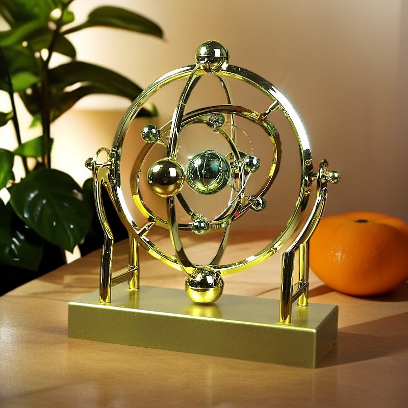 Gold atom model sculpture on a wooden surface with an orange and plant in the background
