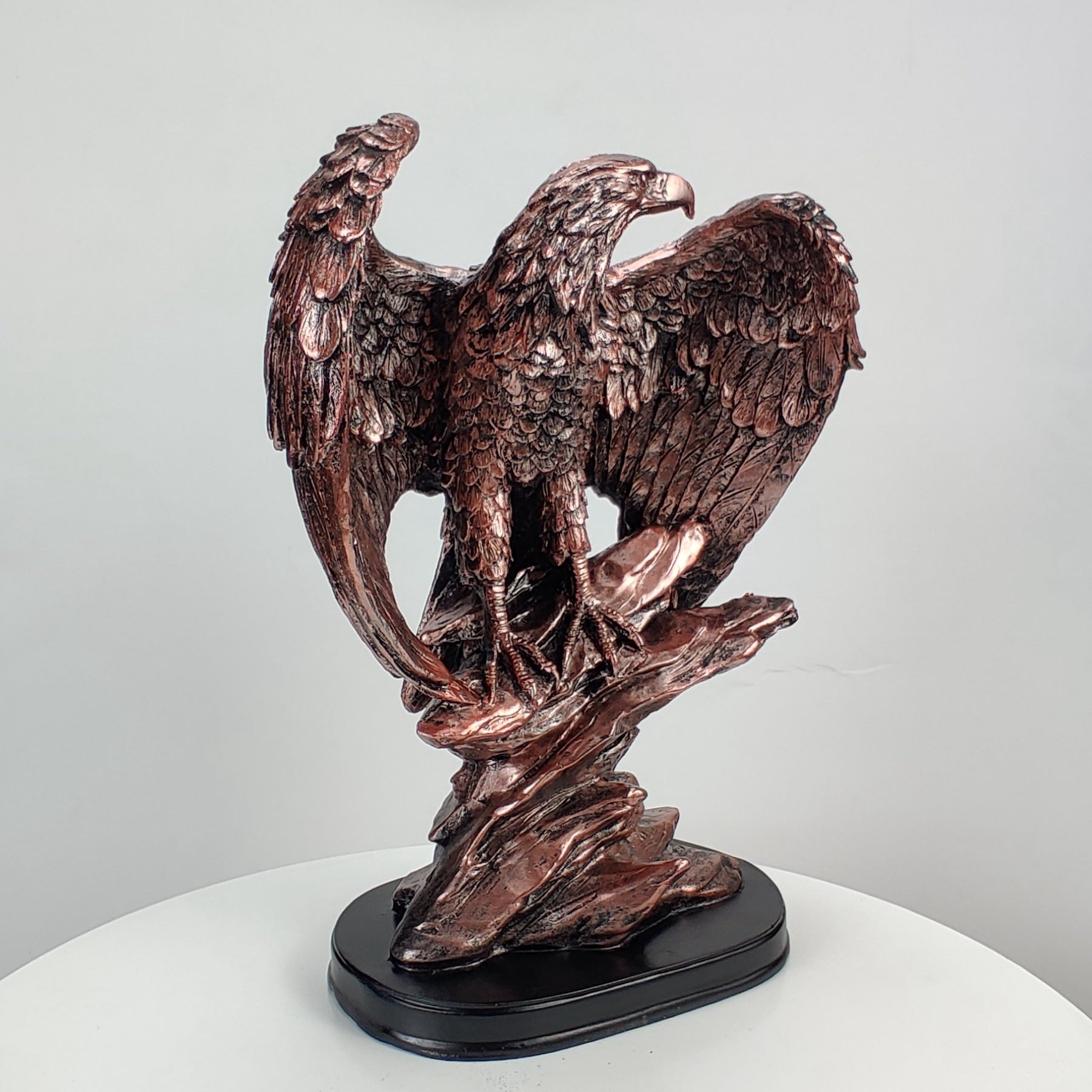 Bronze statue of an eagle on a white pedestal with a light gray background