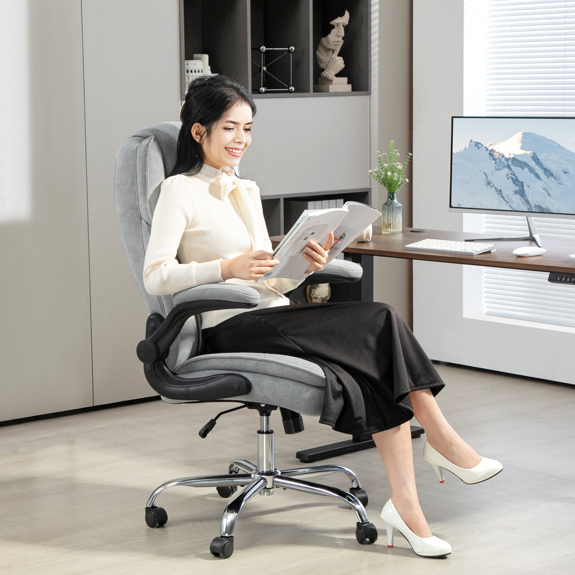 Woman sitting on a gray office chair in an office setting, reading a document.