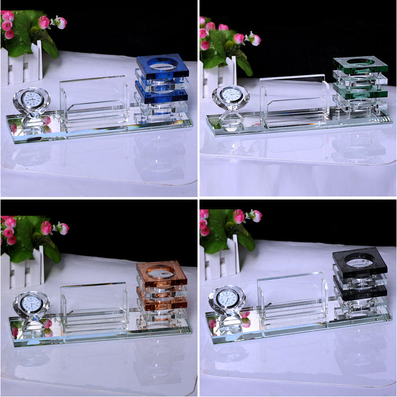 Set of crystal desk accessories with clock and other items on a white surface with flowers in the background.