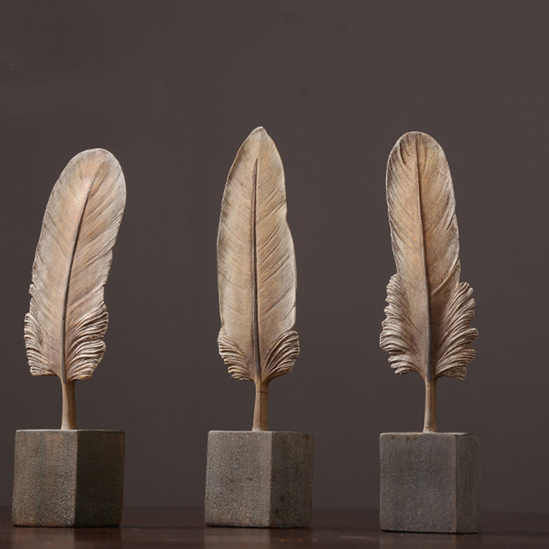 Three feather-shaped sculptures on square bases against a dark background