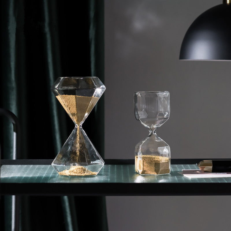 Two geometric hourglasses with gold sand on a dark surface.