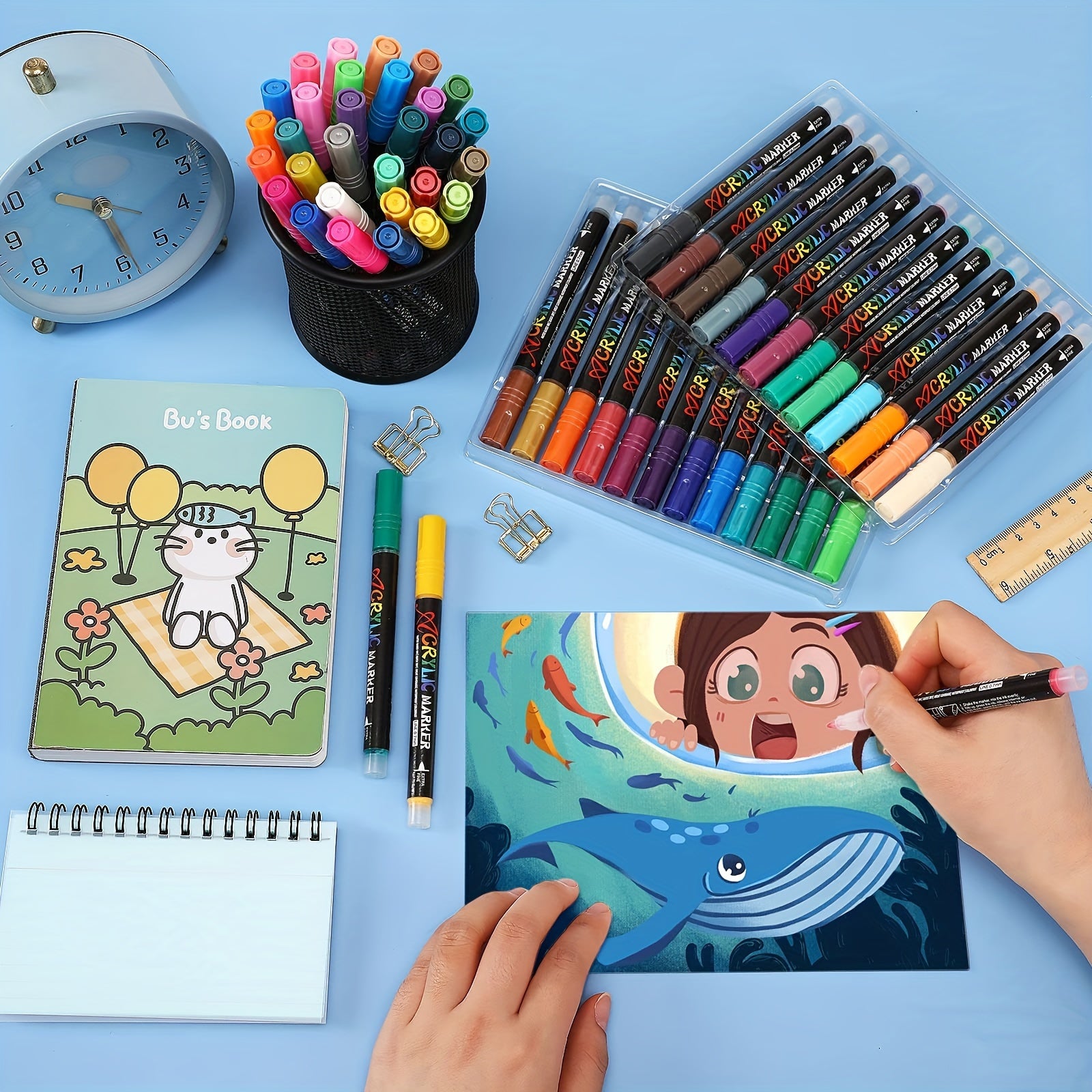 Coloring book with whale and fish design, markers, and stationery on a blue background