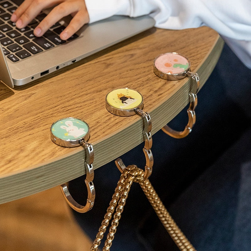 Desk with a laptop and decorative keychain with cartoon characters on a wooden surface.