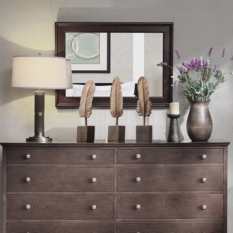 Wooden dresser with decorative items including a lamp, mirror, and flowers.