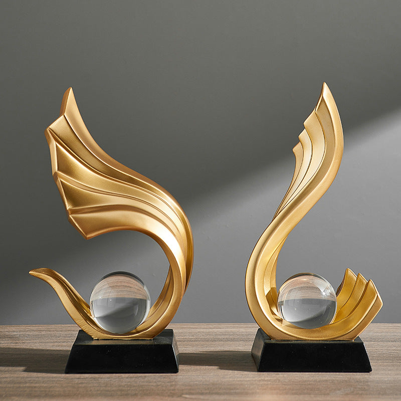 Two gold decorative sculptures with glass spheres on a wooden surface and gray background